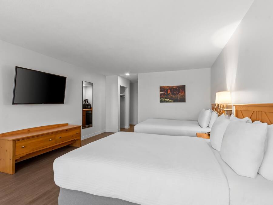 A hotel room with a large bed, a TV mounted on the wall, a wooden dresser, and a painting on the wall.