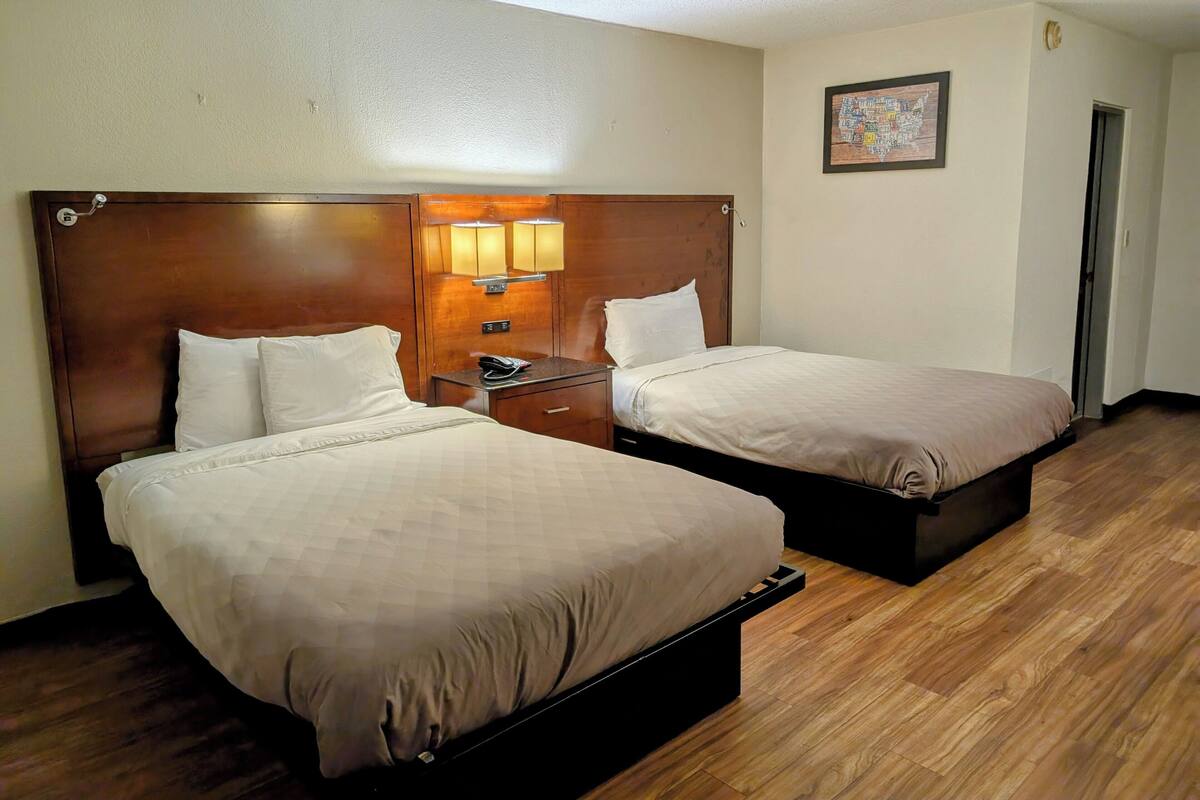 Une chambre d’hôtel avec deux lits, des têtes de lit en bois, une table de chevet avec une lampe et un tableau encadré au mur.