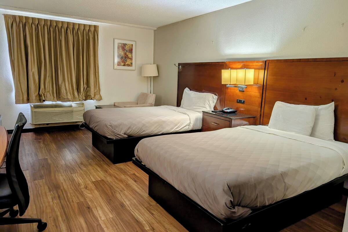 Une chambre d’hôtel avec deux lits, un bureau, une chaise, une lampe et un tableau au mur.
