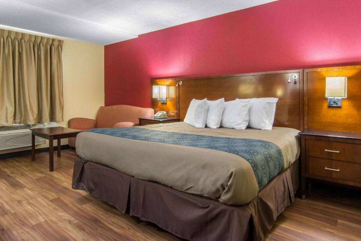 Une chambre d’hôtel avec un lit, un bureau, une chaise, une table de chevet et une lampe.