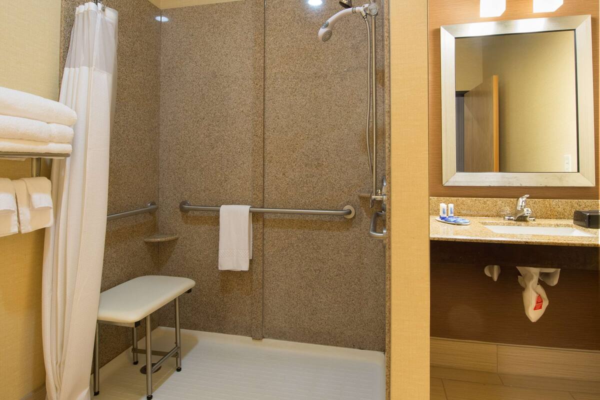 Un baño con ducha, una banca, toallero, lavabo y espejo.