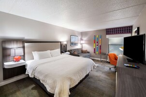 Habitación de hotel con una cama grande, un escritorio con televisor, una silla y una ventana con vistas.