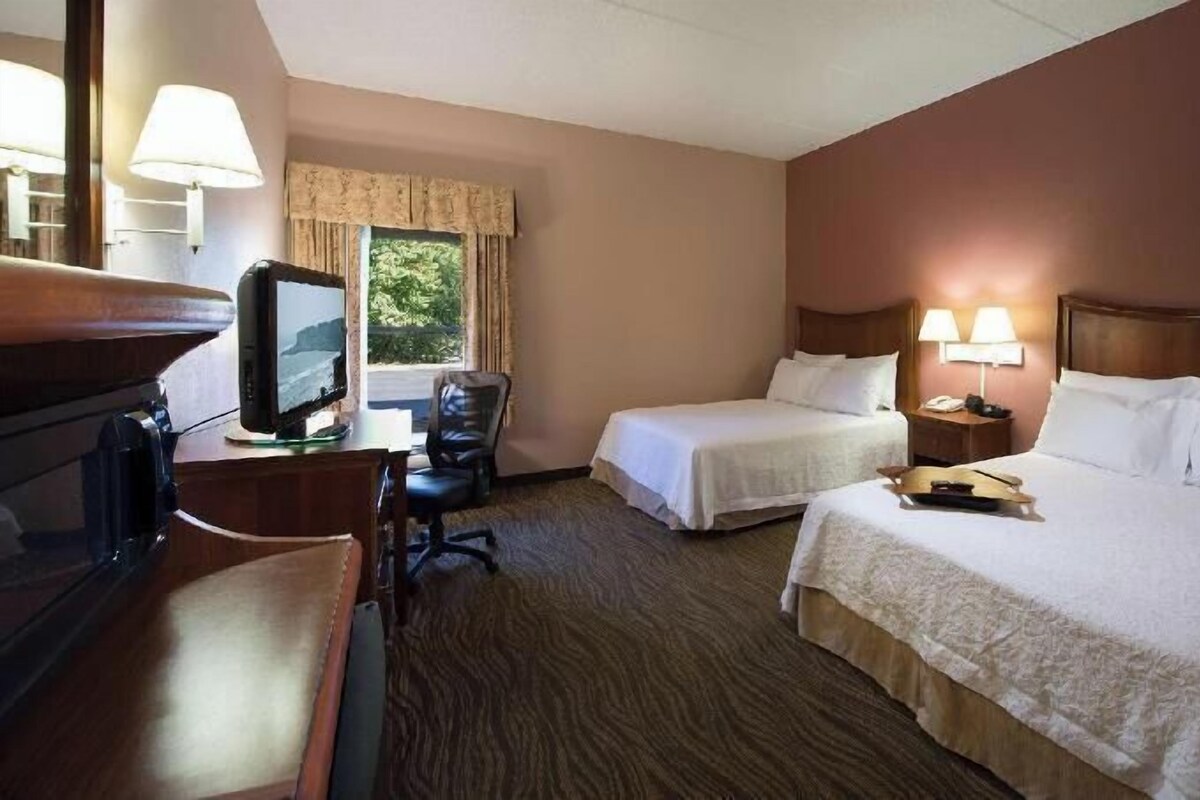 Una habitación de hotel con dos camas, un escritorio con computadora, una silla y un televisor.