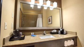Une salle de bain d’hôtel avec un grand miroir, un lavabo, une machine à café et des serviettes.