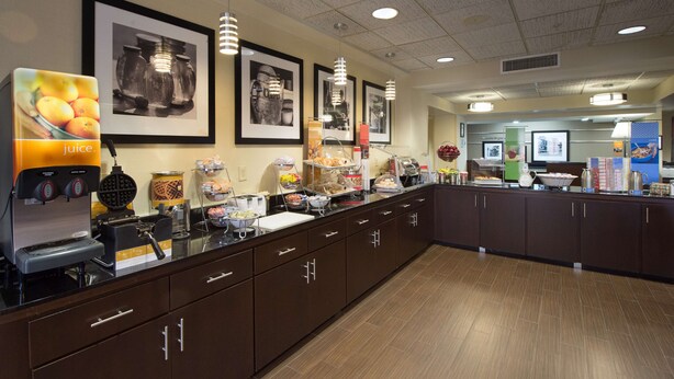 A breakfast bar with juice dispensers, a waffle maker, and various food items. - Hampton Inn Gainesville (Gainesville)