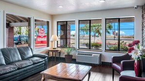 A hotel lobby with a leather sofa, a wooden coffee table, and a red vase with flowers. - Red Roof Inn Palmdale - Lancaster (Palmdale)