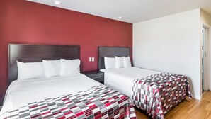 Une chambre d’hôtel avec deux lits, un mur d’accent rouge et un plafond blanc.