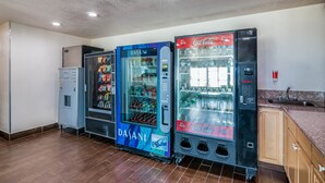 Une cuisine équipée de trois distributeurs automatiques de boissons, d’un réfrigérateur et d’un évier.