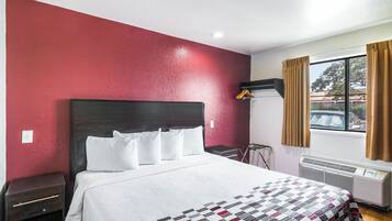 A hotel room with a bed, a bedside table, a hanging light, a window with curtains, and a radiator.