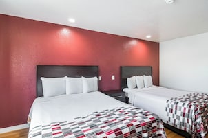 Habitación de hotel con dos camas, una pared de acento roja y un techo blanco.