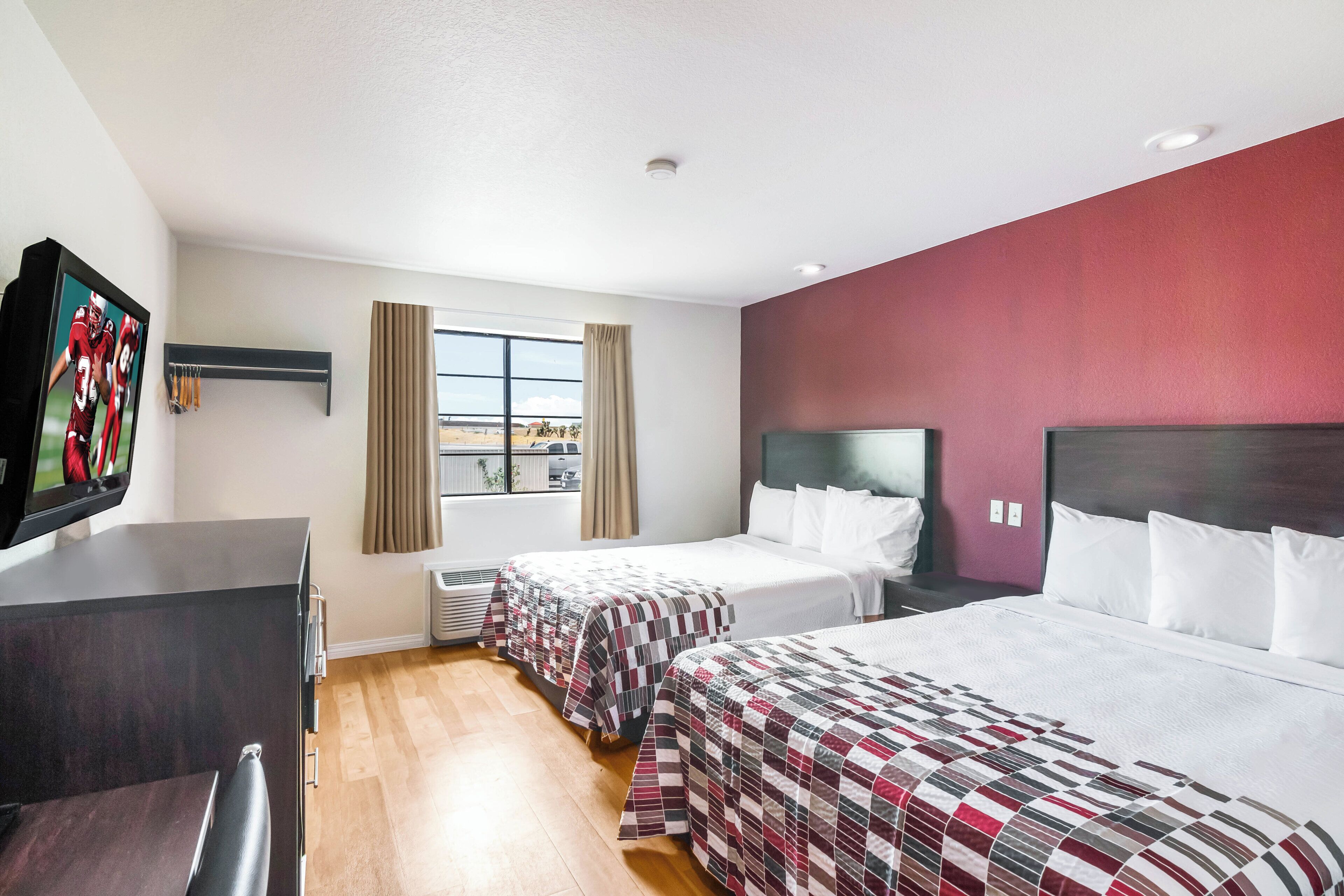 Habitación de hotel con dos camas, un escritorio, un televisor y un ventanal con cortinas.