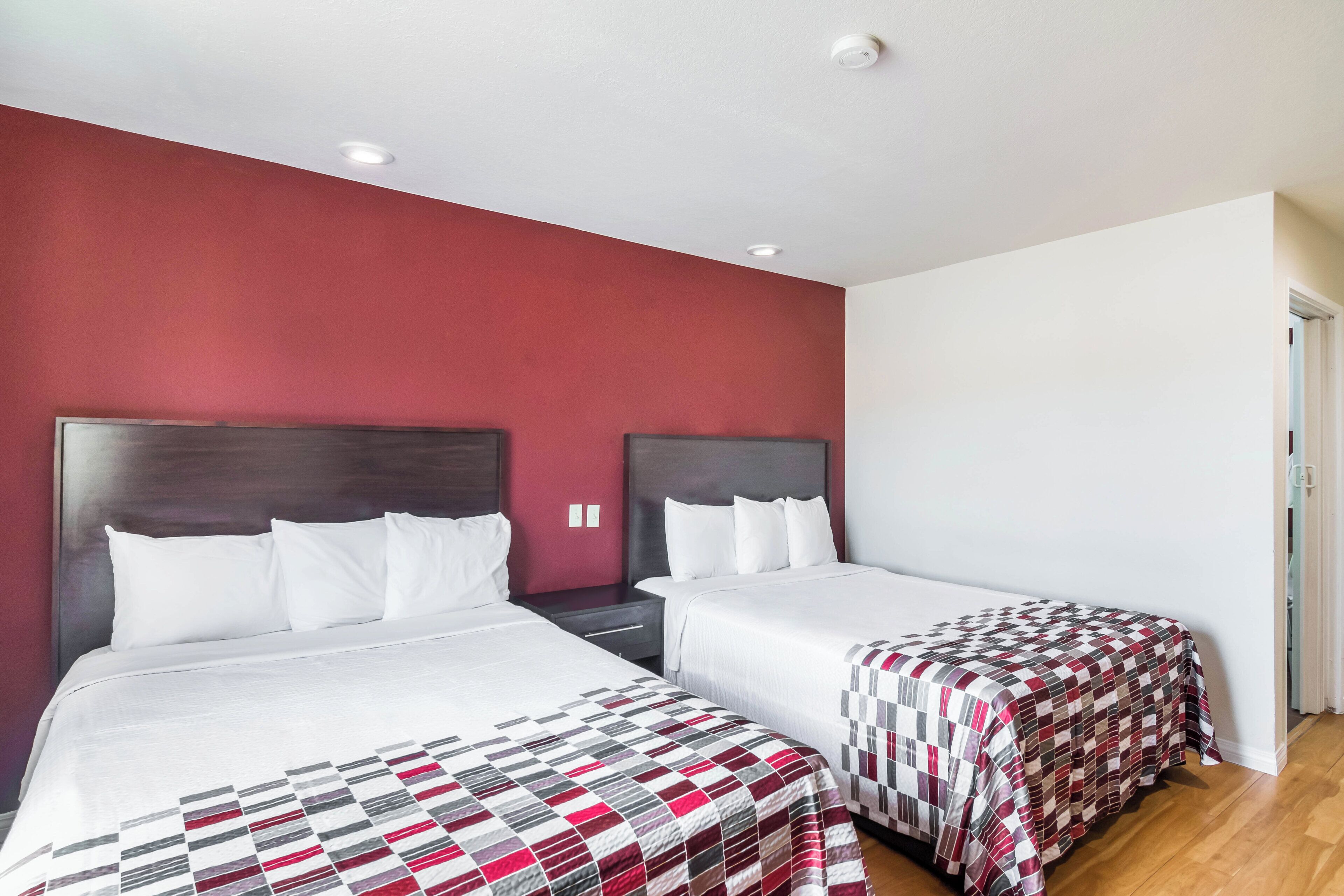A hotel room with two beds, a red accent wall, and a white ceiling.