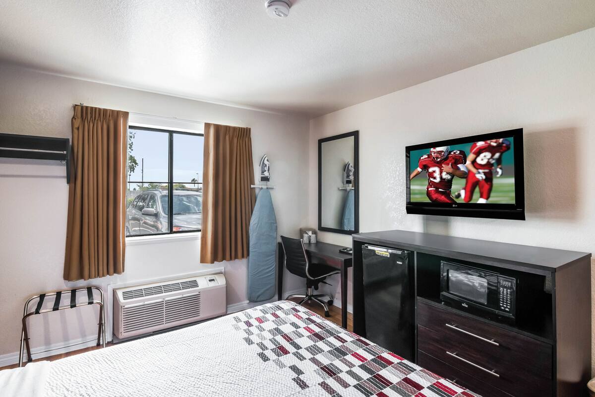 A hotel room with a bed, a desk, a chair, a TV, and a microwave.