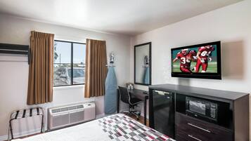 A hotel room with a bed, a desk, a television, a mirror, and a window with curtains.