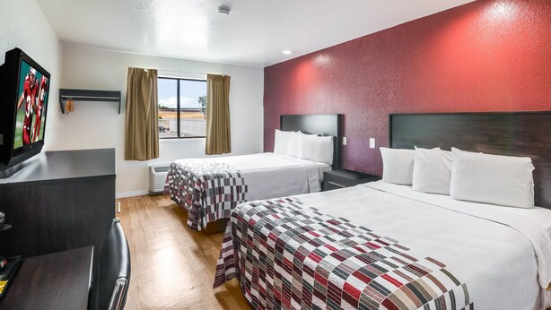 Une chambre d’hôtel avec deux lits, une télévision, un bureau et une fenêtre avec des rideaux.