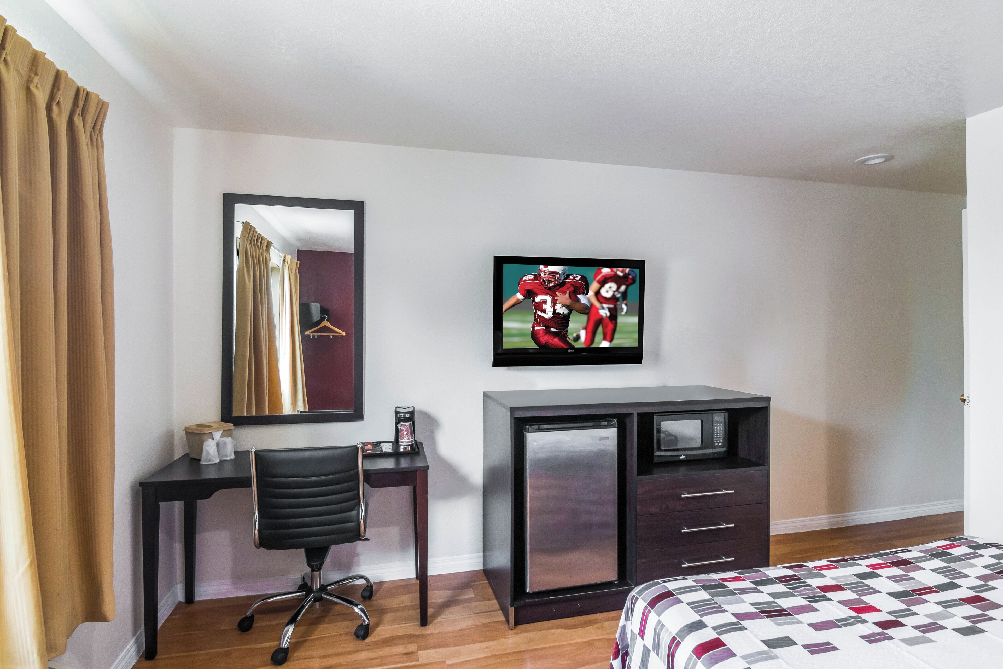 Een hotelkamer met een bed, een bureau met stoel, een televisie en een minibar.