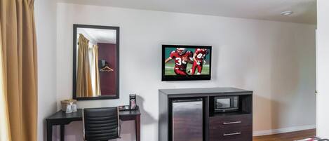 Una habitación de hotel con una cama, un escritorio con una silla, un televisor y un mini bar.