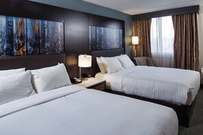 A hotel room with two beds, a large abstract painting on the wall, a bedside table with a lamp, and a view of the city through large windows. - DoubleTree by Hilton Neenah (Neenah)