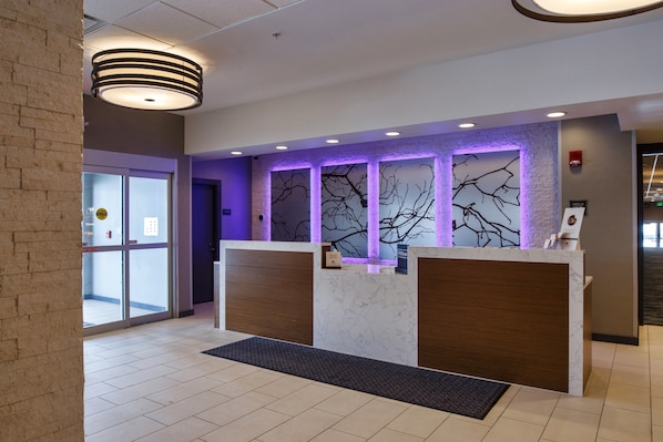 A modern reception desk with a marble top and wooden panels, flanked by glass doors. - DoubleTree by Hilton Neenah (Neenah)