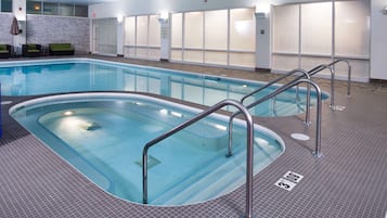 A swimming pool with metal railings, tiled flooring, and a brick wall with a sign.