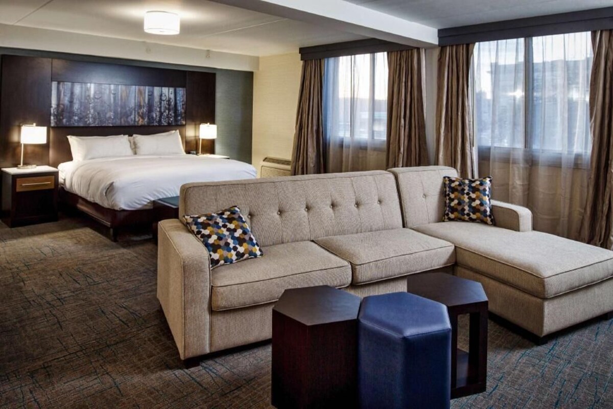A hotel room with a large bed, a sofa, two side tables, and a large window with curtains.