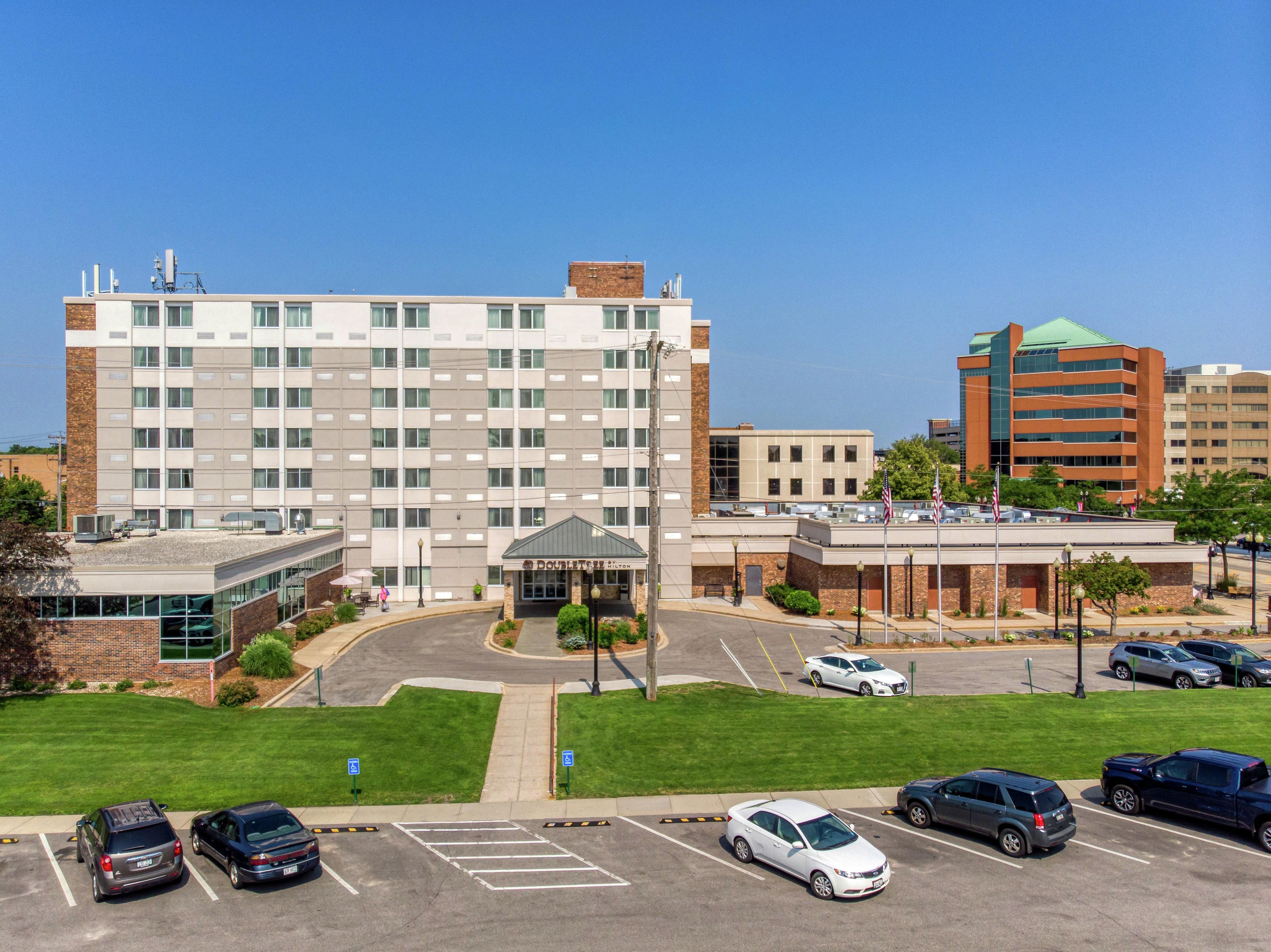 A multi-story hotel with a central courtyard, parking lot, and various buildings in the background.