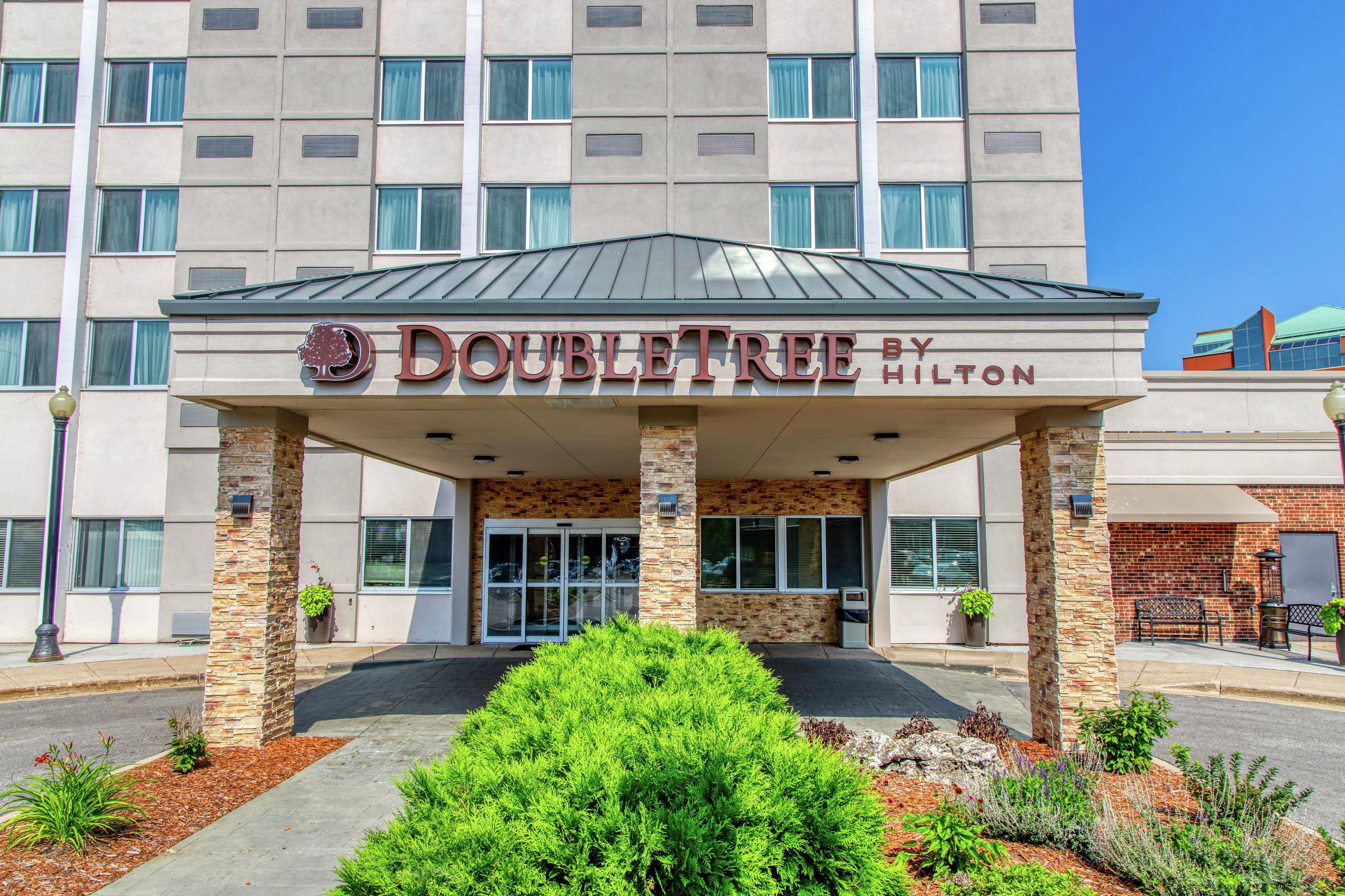 A DoubleTree by Hilton hotel entrance with a brick facade, large windows, and a covered entrance area.