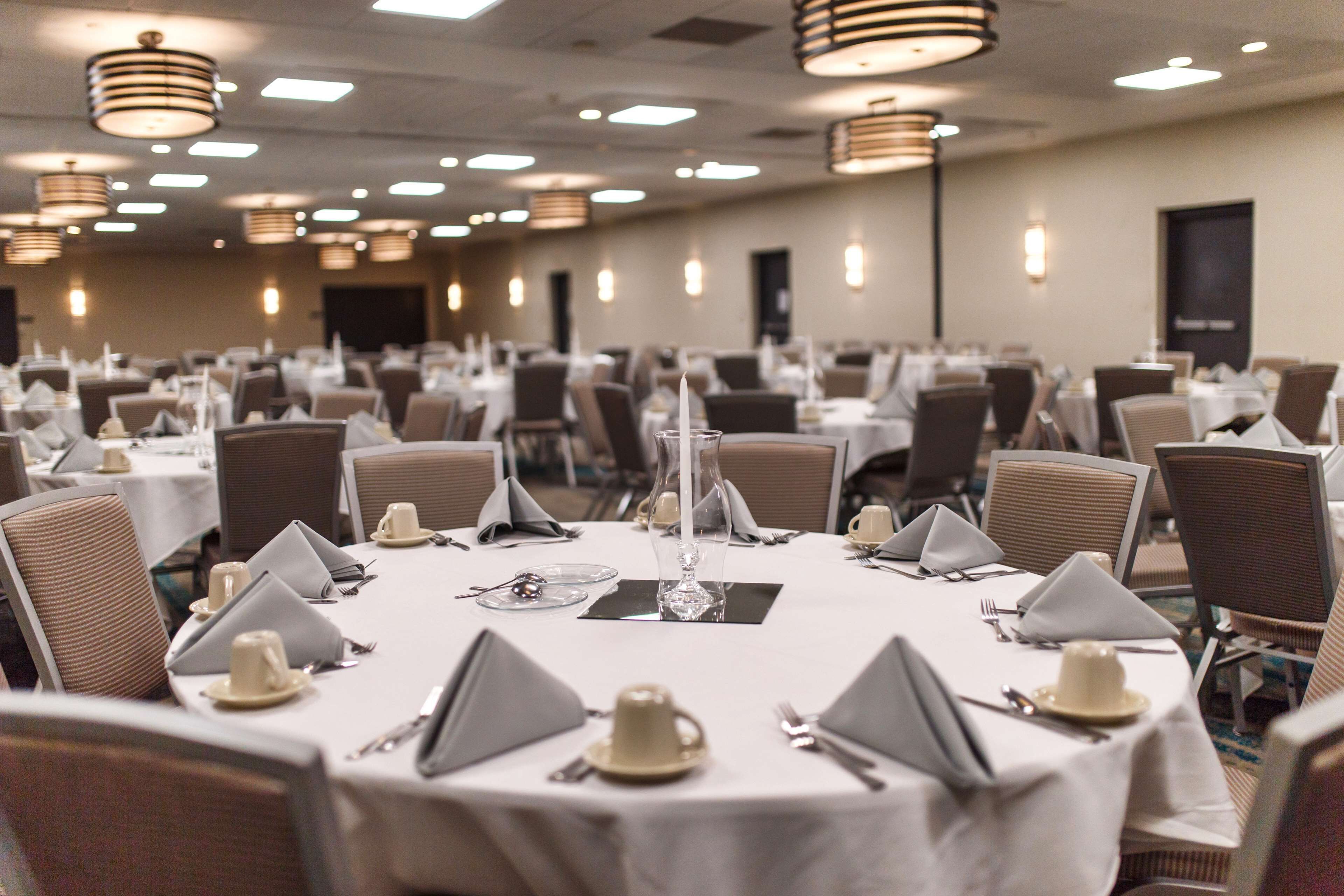 Un salón de banquetes con mesas redondas dispuestas para comer, equipado con manteles blancos, servilletas y cubiertos.