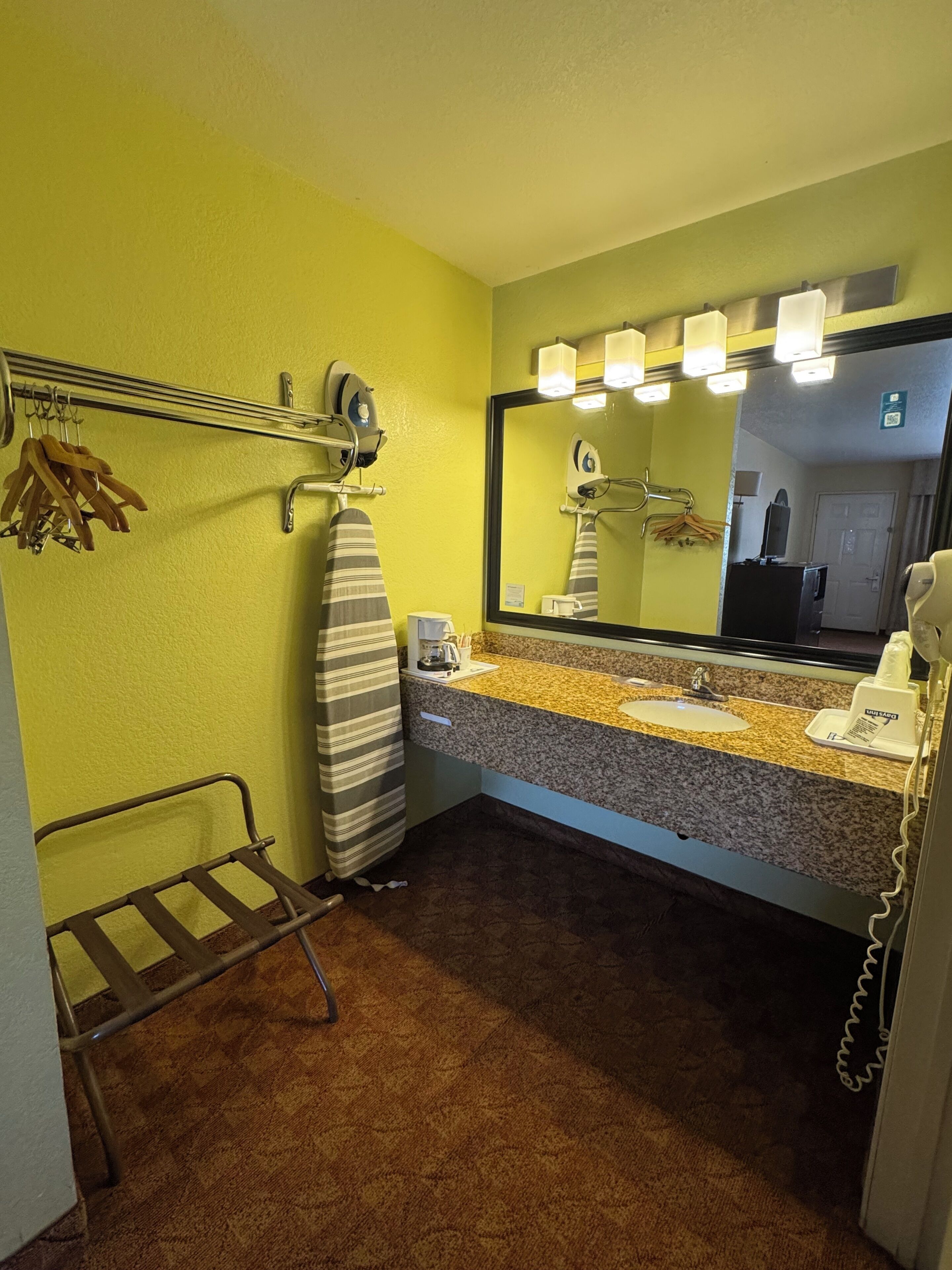 Een hotelbadkamer met een granieten aanrecht, een wastafel, een spiegel met verlichting, een strijkijzer en een handdoekhouder.