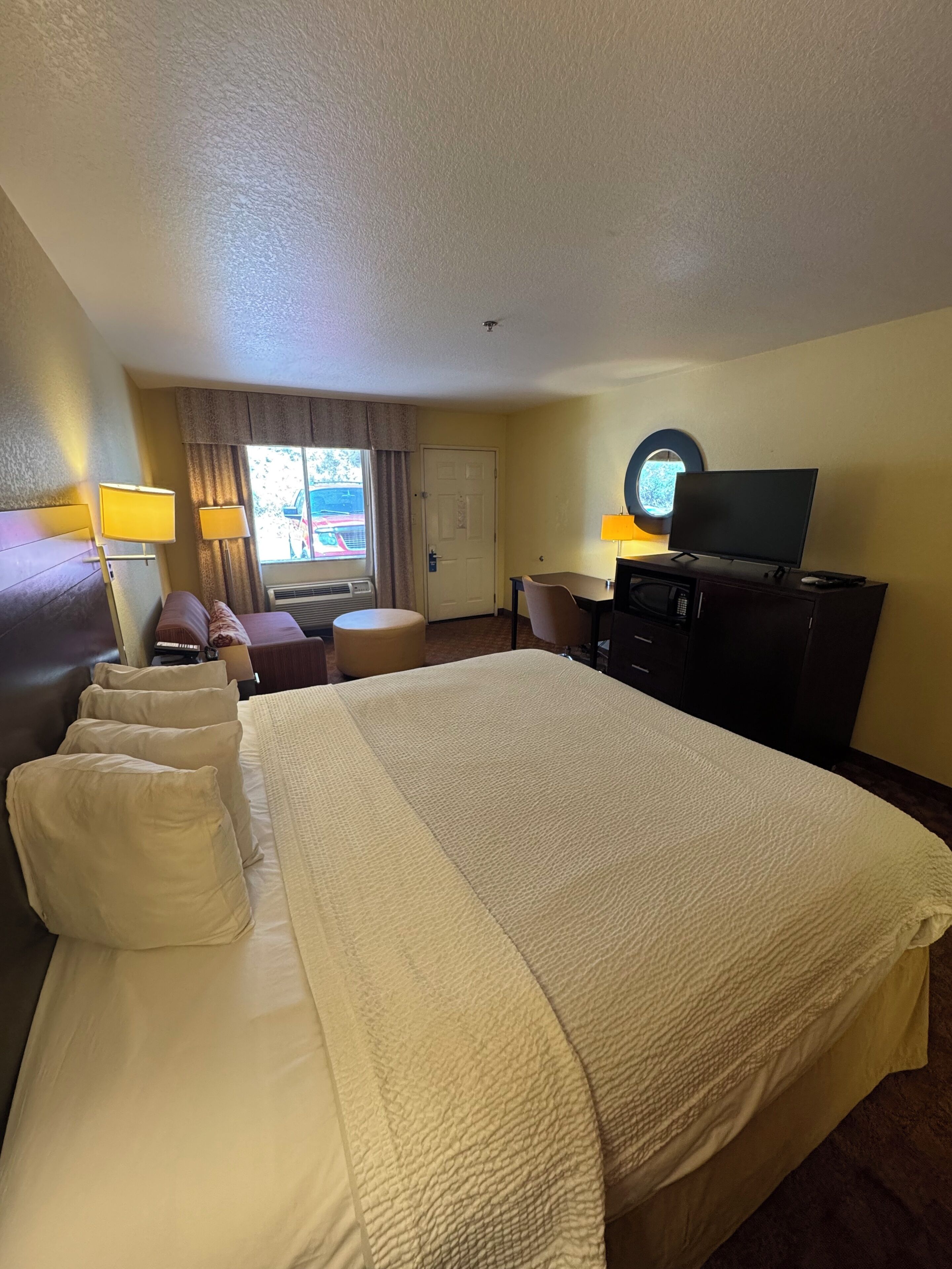 Een hotelkamer met een groot bed, een bureau, een televisie en een raam met gordijnen.
