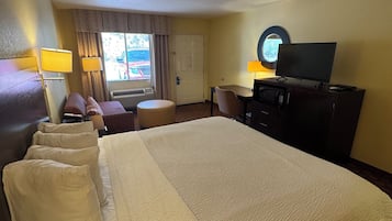 Een hotelkamer met een groot bed, een bureau, een televisie en een raam met gordijnen.