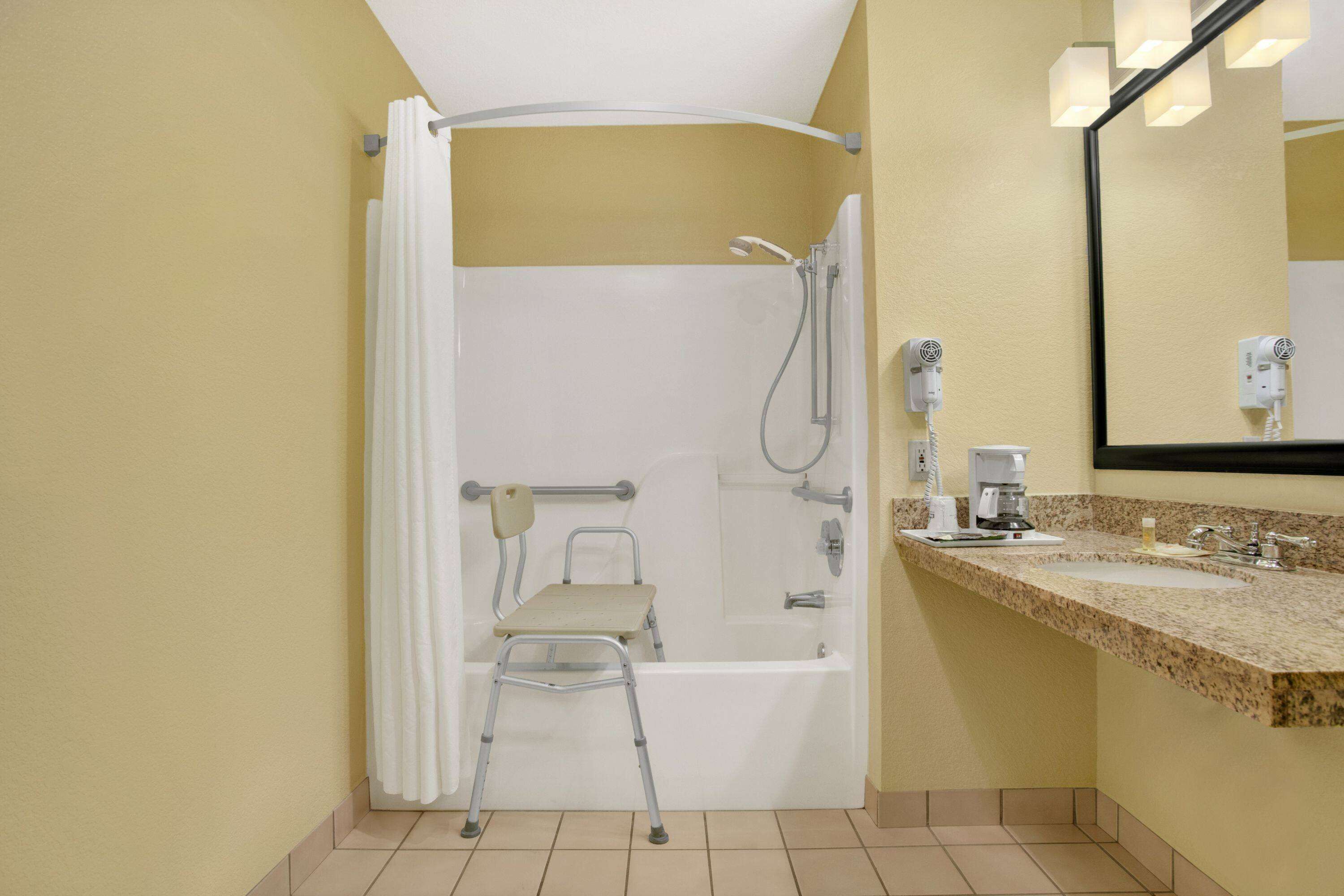 A bathroom with a shower, a chair, a sink, and a mirror.