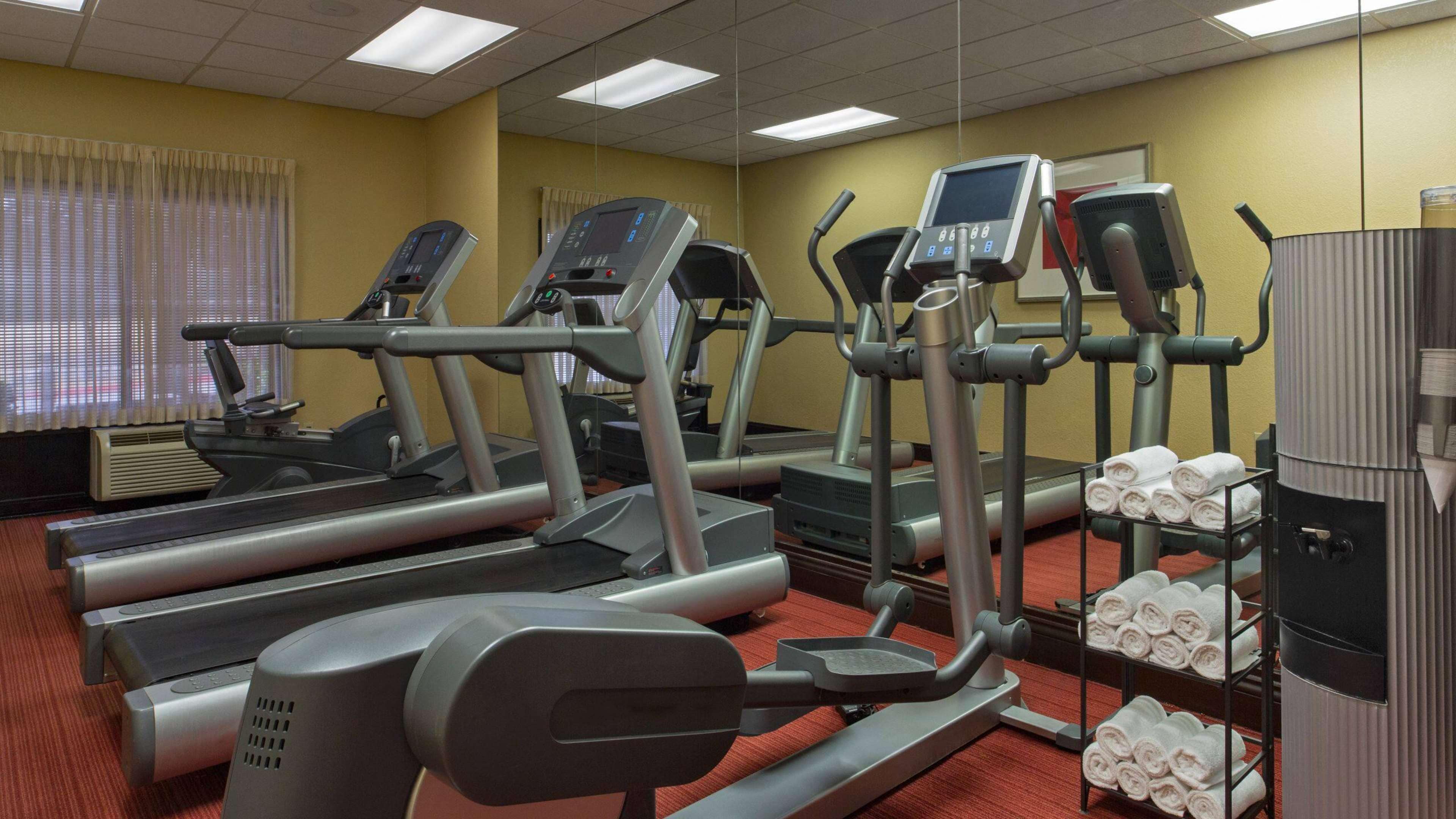 Un gimnasio con cintas de correr, elípticas y un perchero con toallas.