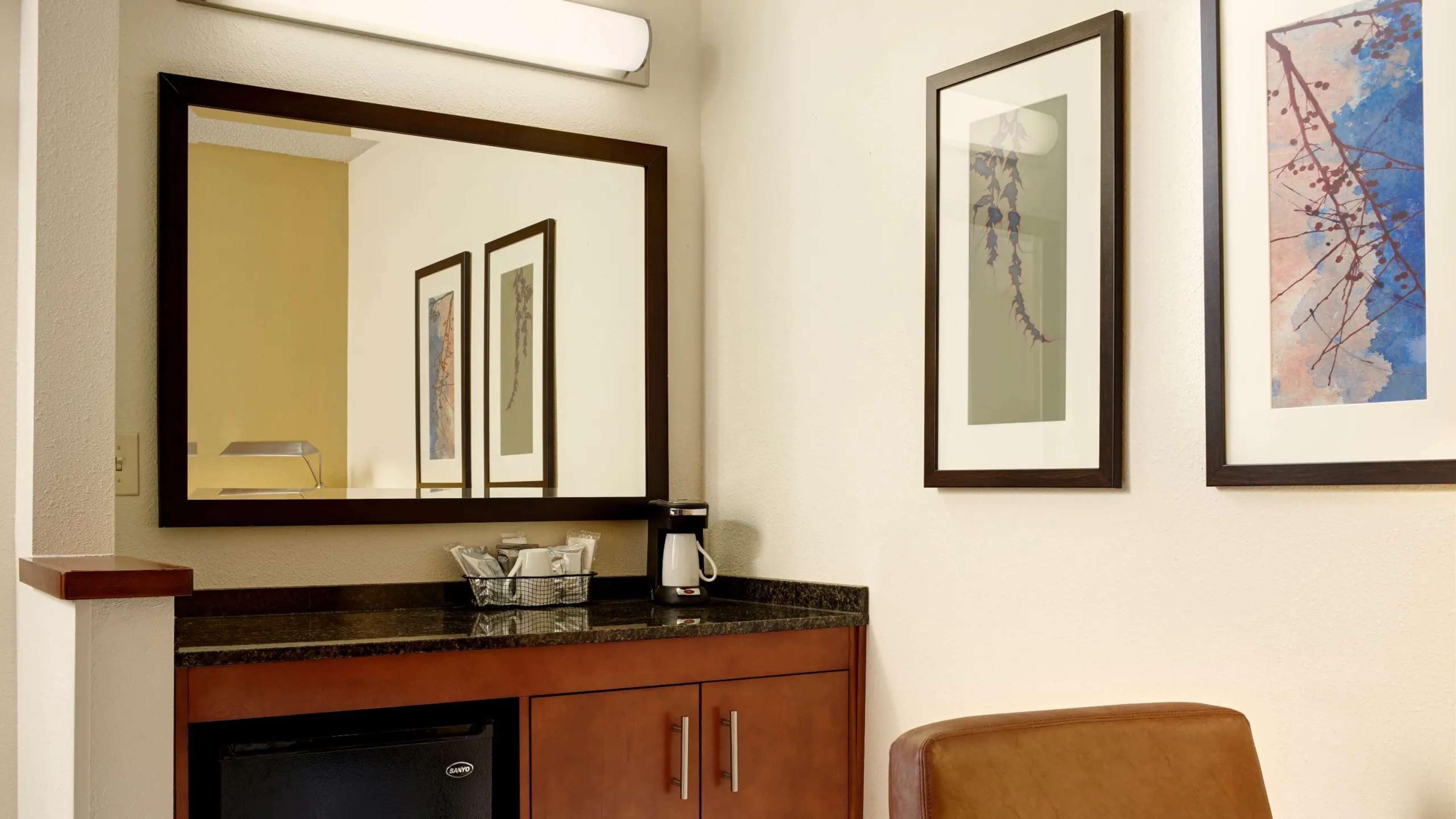 Un baño con un espejo grande, obras de arte enmarcadas, una cafetera y un armario.