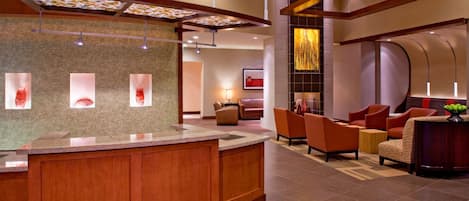 A modern lobby with a reception desk, seating area, and a decorative wall with abstract art.