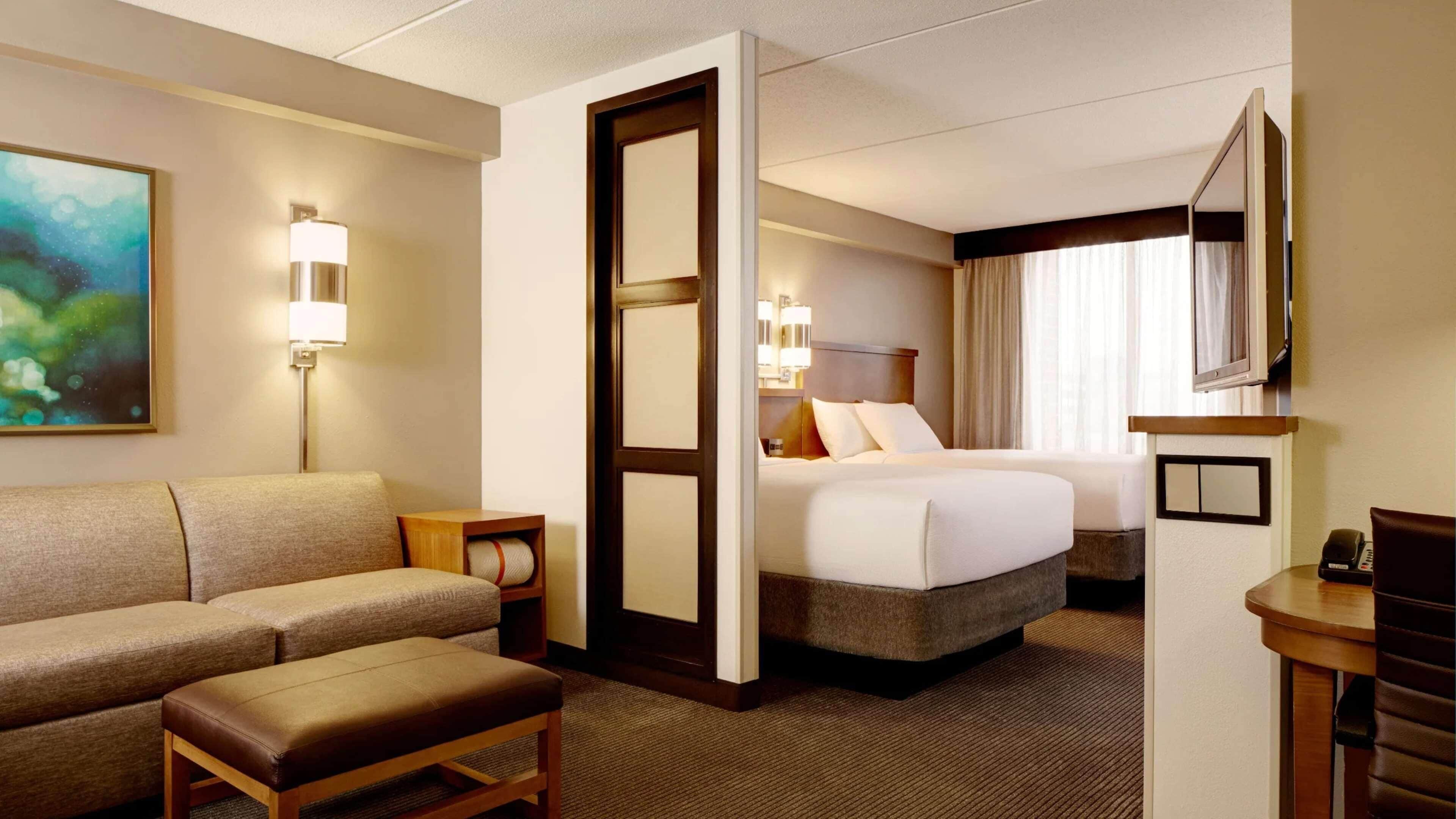 A hotel room with a sofa, a bed, a desk, a mirror, and a painting on the wall.