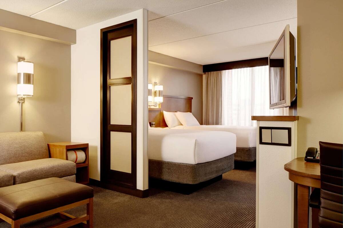 A hotel room with a sofa, a bed, a desk, a mirror, and a painting on the wall.