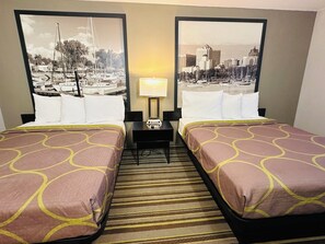 A hotel room with two beds, a nightstand, a lamp, and a view of a marina and cityscape through large windows.