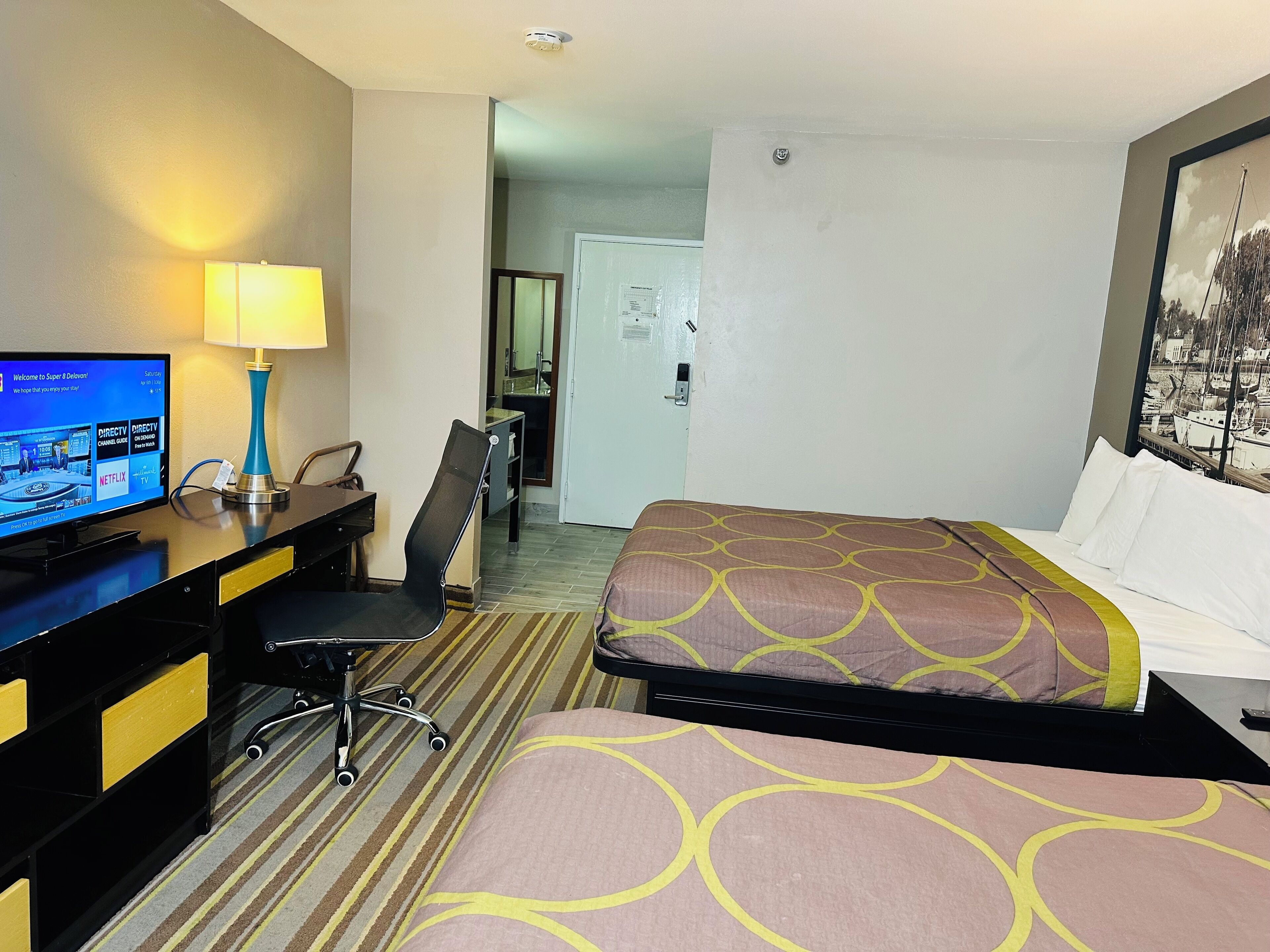 Ein Hotelzimmer mit einem Bett, einem Schreibtisch mit Computer, einem Stuhl und einer Lampe.