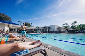 A swimming pool area with lounge chairs, a pool with lane dividers, and a building with a flat roof and windows. - Guesthouse Hotel at La Valle (Rancho Santa Fe)