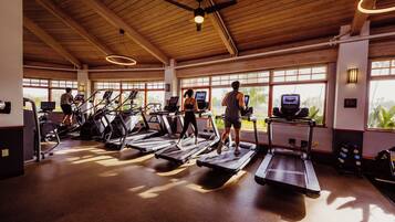 Un gimnasio con cintas de correr, bicicletas estáticas y un ventilador de techo.