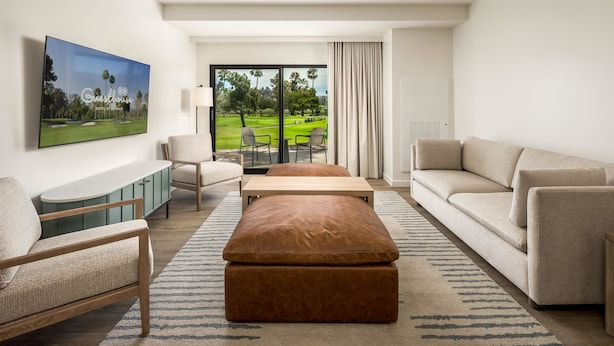 Una habitación de hotel moderna con un ventanal grande, un sofá, una mesa de centro, un televisor y un armario.