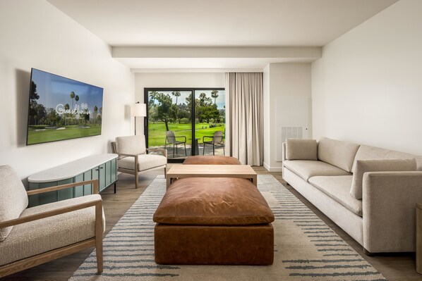 A modern hotel room with a large window, a sofa, a coffee table, a TV, and a cabinet. - Guesthouse Hotel at La Valle (Rancho Santa Fe)