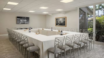 Un salón de conferencias con una larga mesa, sillas, una pantalla de proyector y un cuadro.