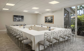 Een vergaderzaal met een lange tafel, stoelen, een projectorscherm en een schilderij.