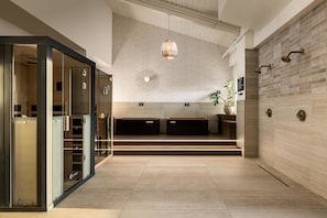 A modern hotel lobby with a glass partition, a reception desk, a hanging light fixture, and a wall-mounted shower.