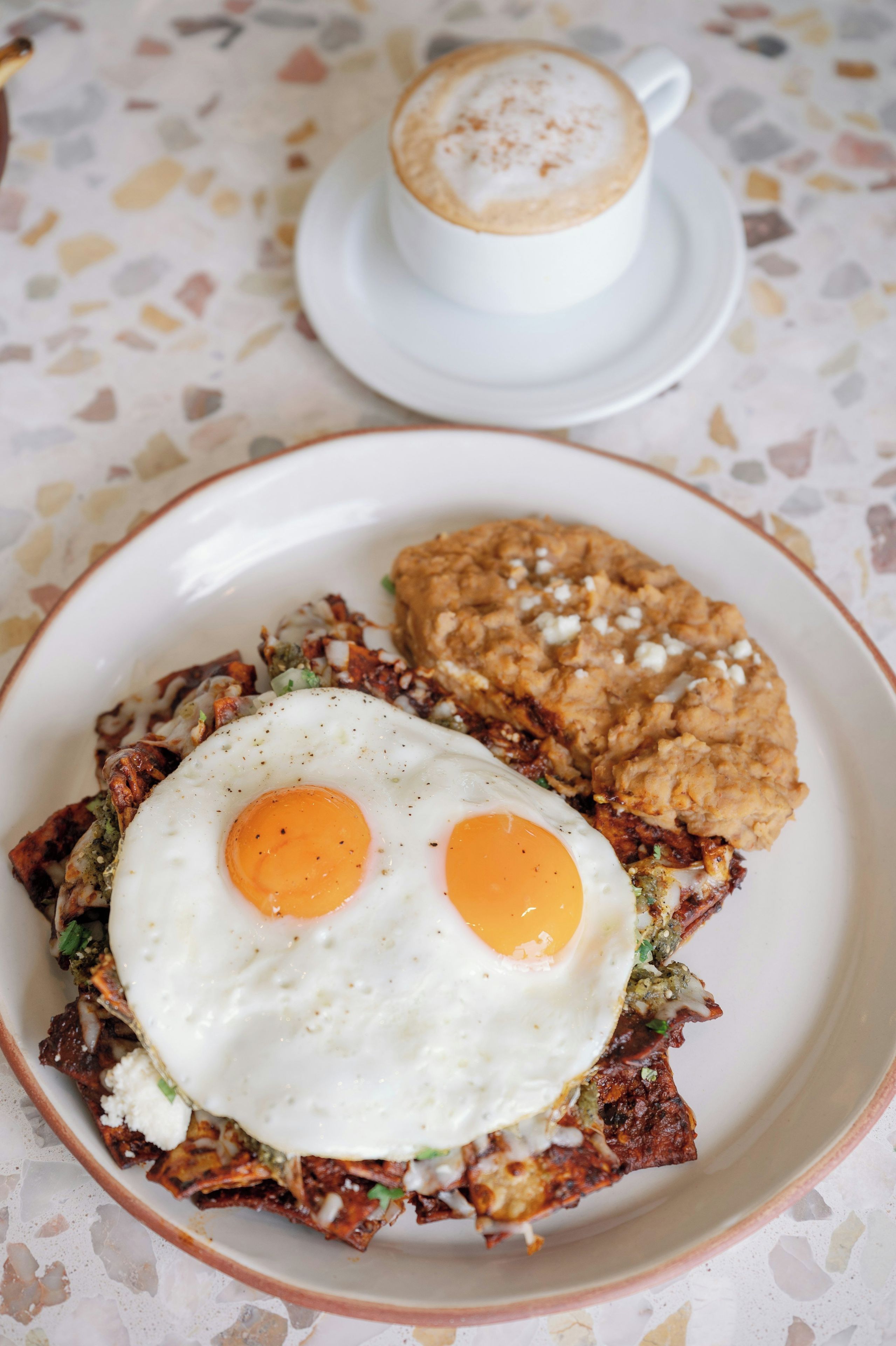 A plate with a fried egg and a hash brown, and a cup of coffee on a table with a speckled surface.