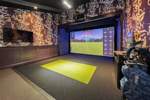 A golf simulation room with a large screen displaying a golf course, a yellow mat, and a golf bag. - Guesthouse Hotel at La Valle (Rancho Santa Fe)