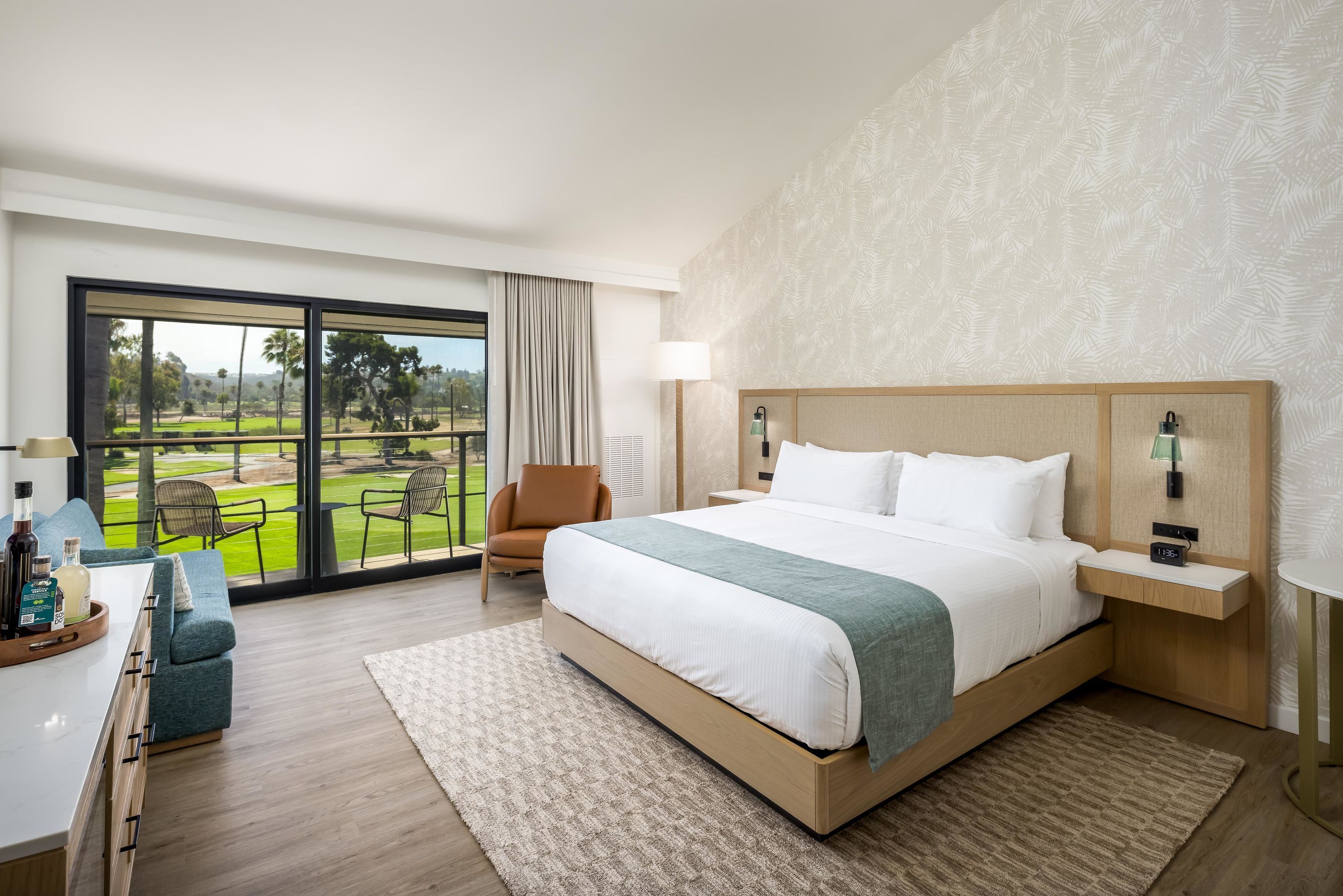 A hotel room with a large bed, a desk with a chair, a window with a view of a golf course, and a nightstand with a lamp.