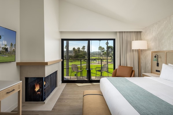 Ein Hotelzimmer mit einem großen Bett, einem Kamin, einem Fernseher und einem Balkon mit Blick auf einen Golfplatz.